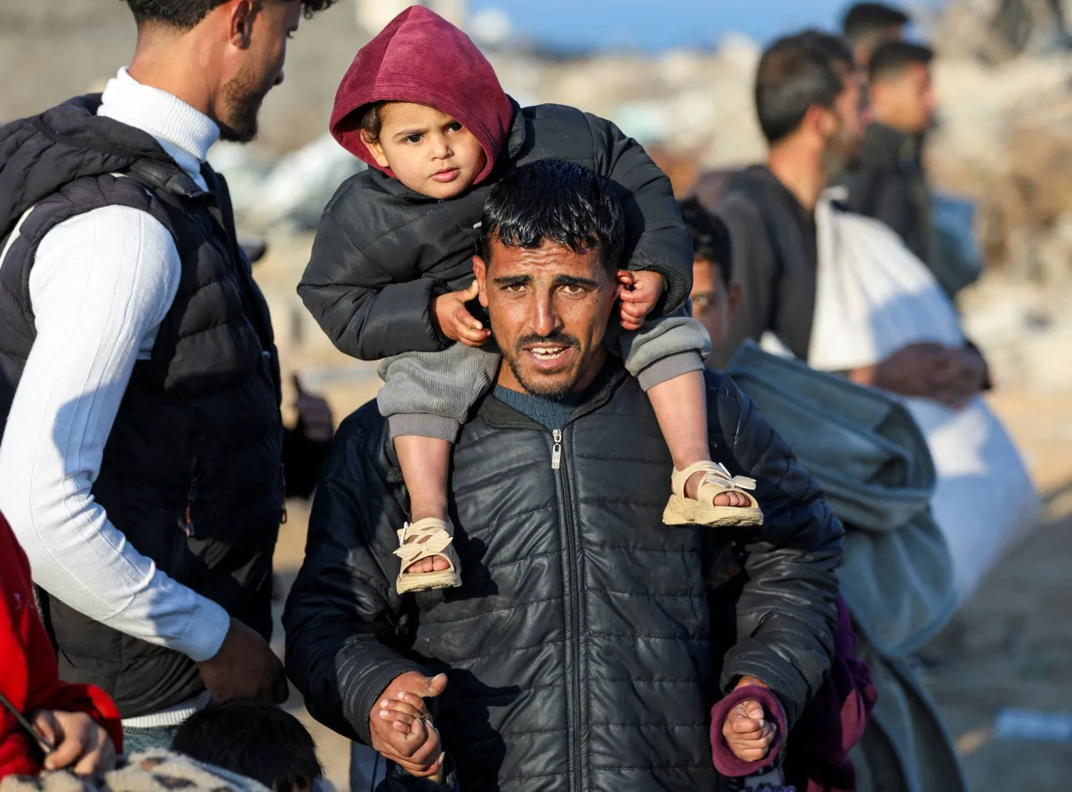 فلسطيني يحمل طفله على كتفيه في طريق العودة إلى منزله بشمال قطاع غزة (رويترز)